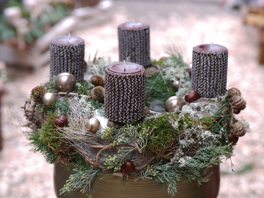 Adventskranz mit vier dunklen, strukturierten Kerzen umgeben von Tannenzweigen, Moos, Zapfen und silbernen Weihnachtskugeln.